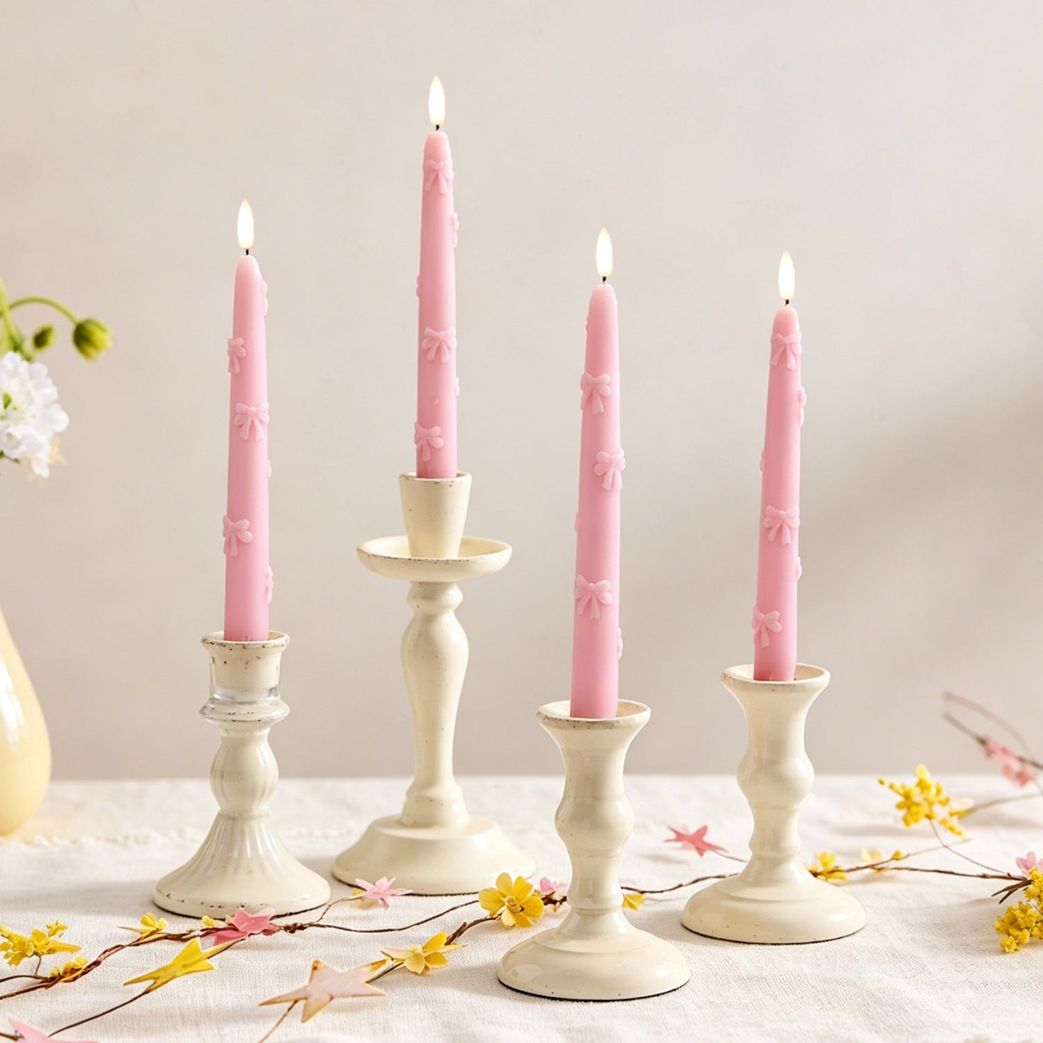 Set of pink candles in white candlesticks on a light surface with floral decorations.