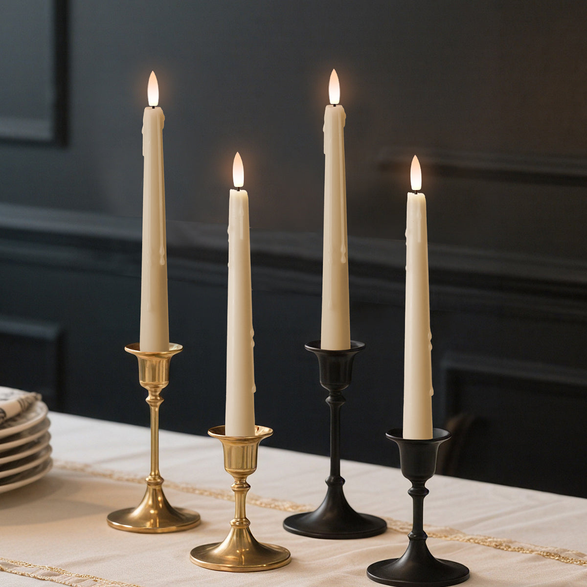A set of three flameless taper candles in gold, black, and bronze colors, with a lifelike glow, displayed on a table.