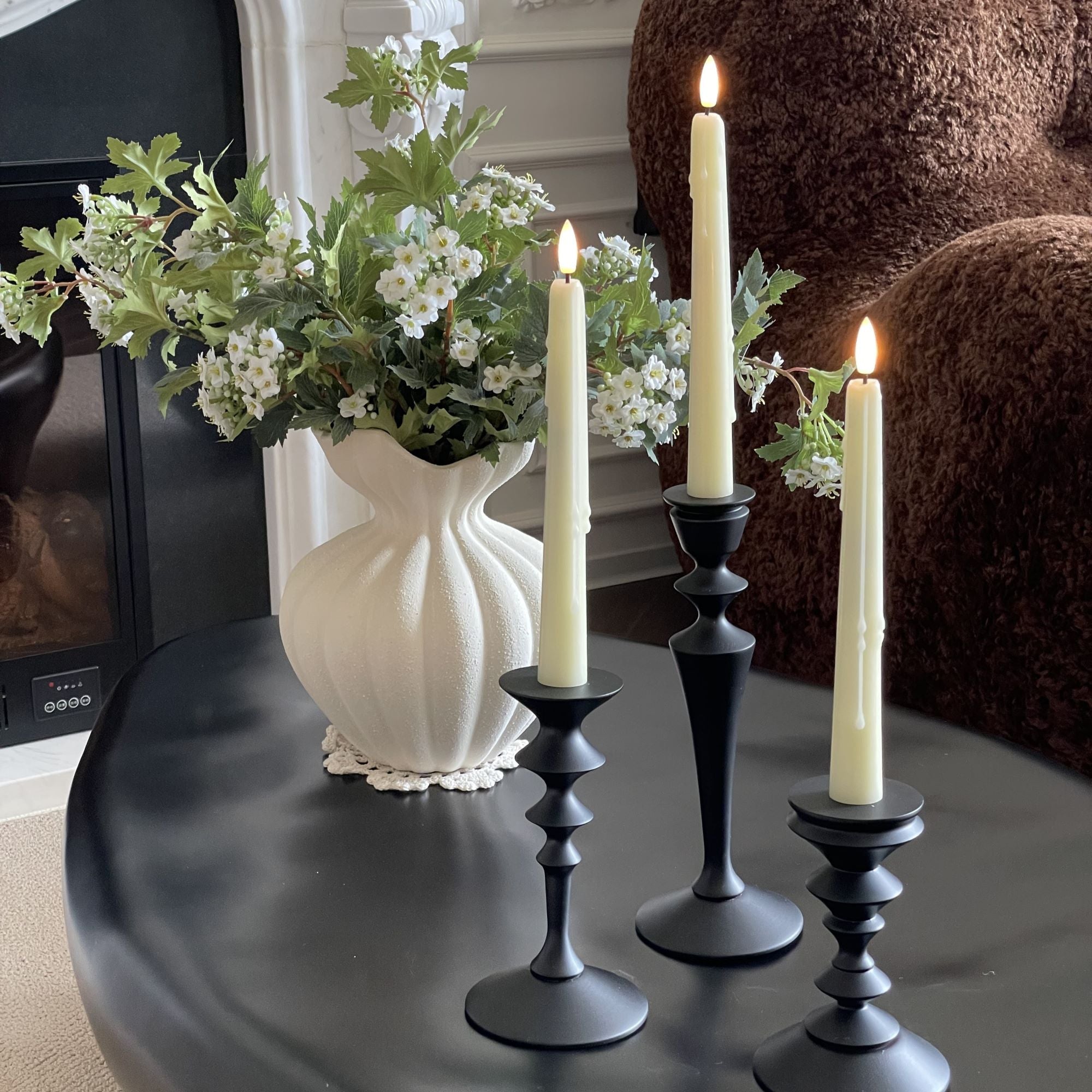 Decorative setup with candles in black holders and a vase of flowers on a table.#color_ivory