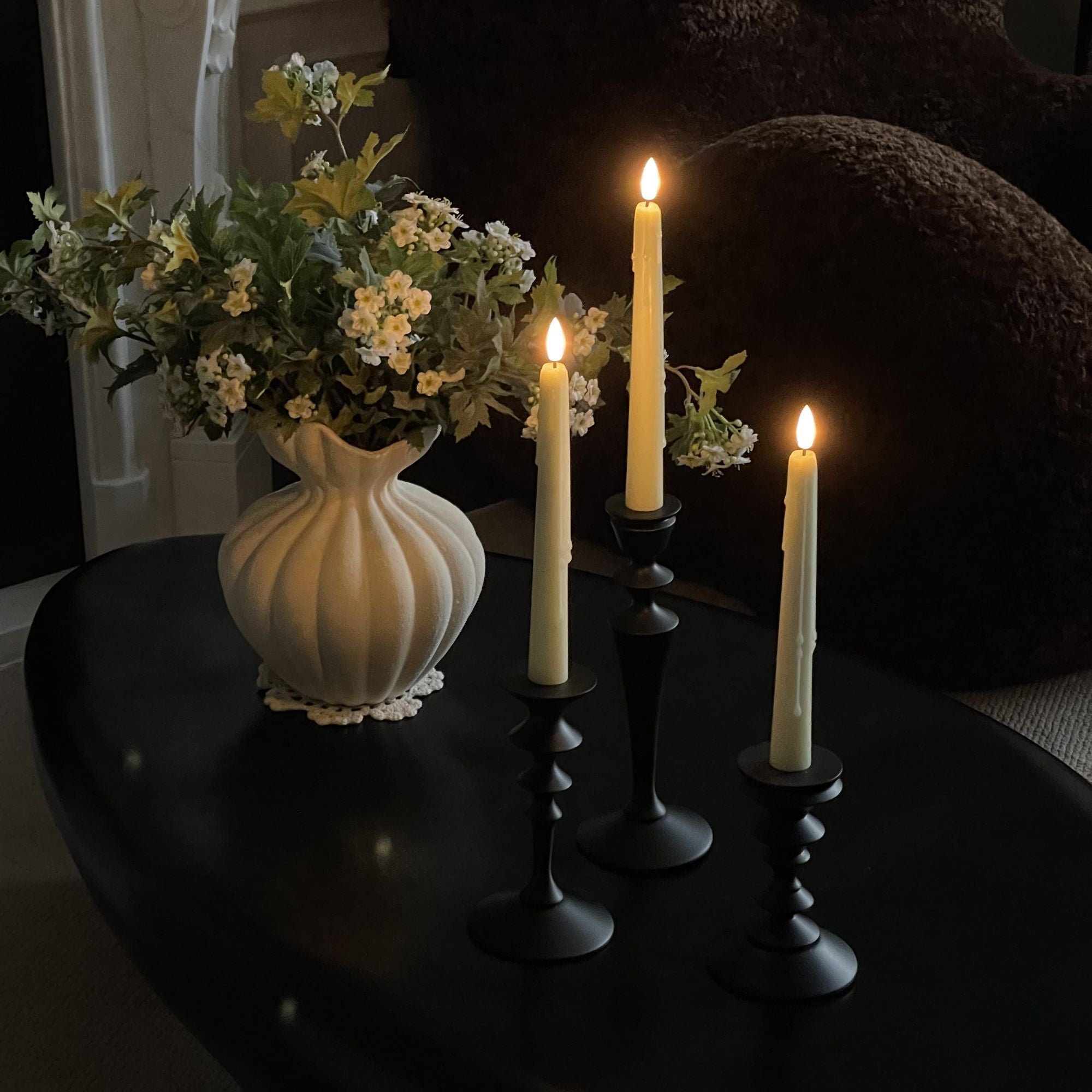 Candlelit scene with a vase of flowers on a dark surface#color_ivory