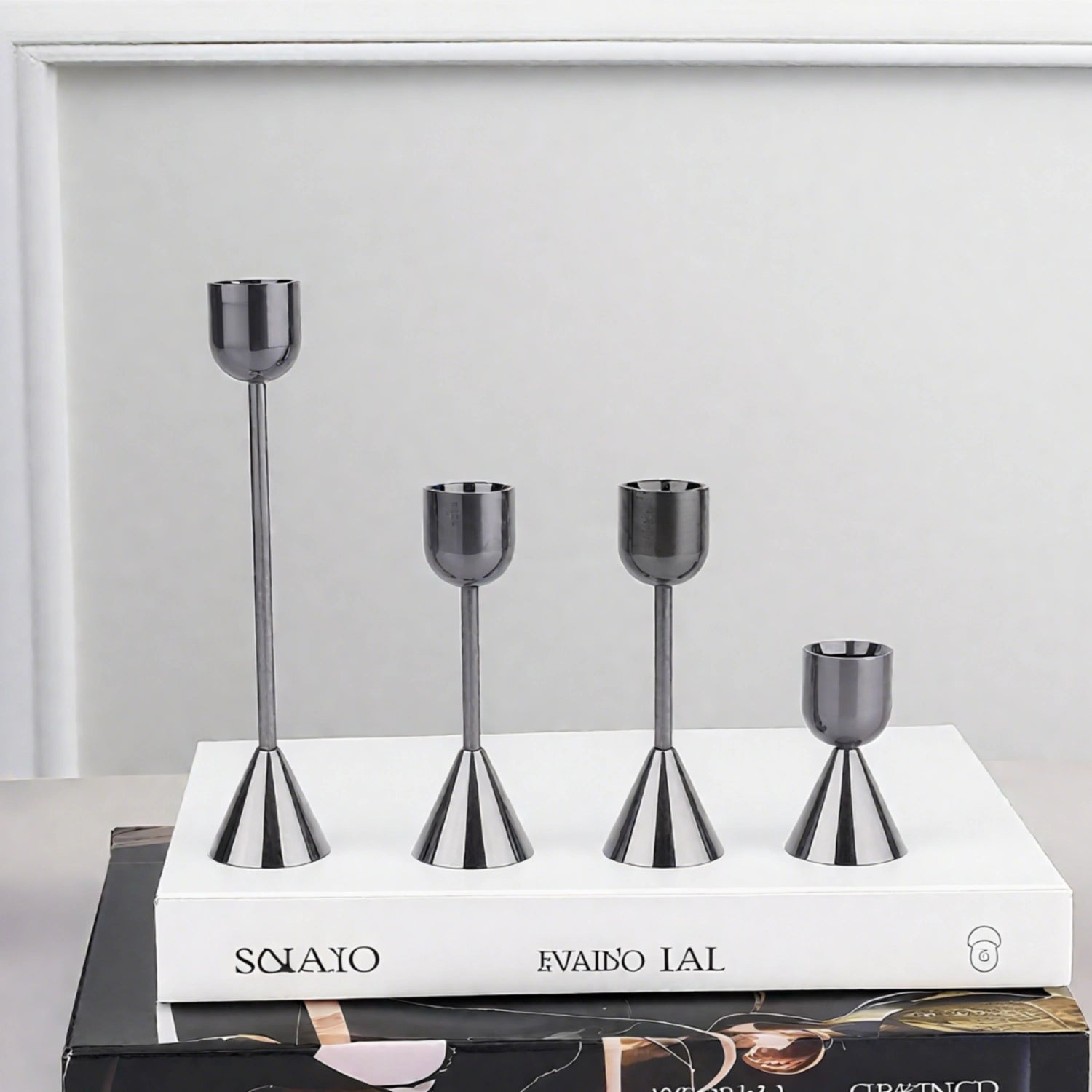 Set of four metallic candle holders on a white book with a gray background#color_metal-black