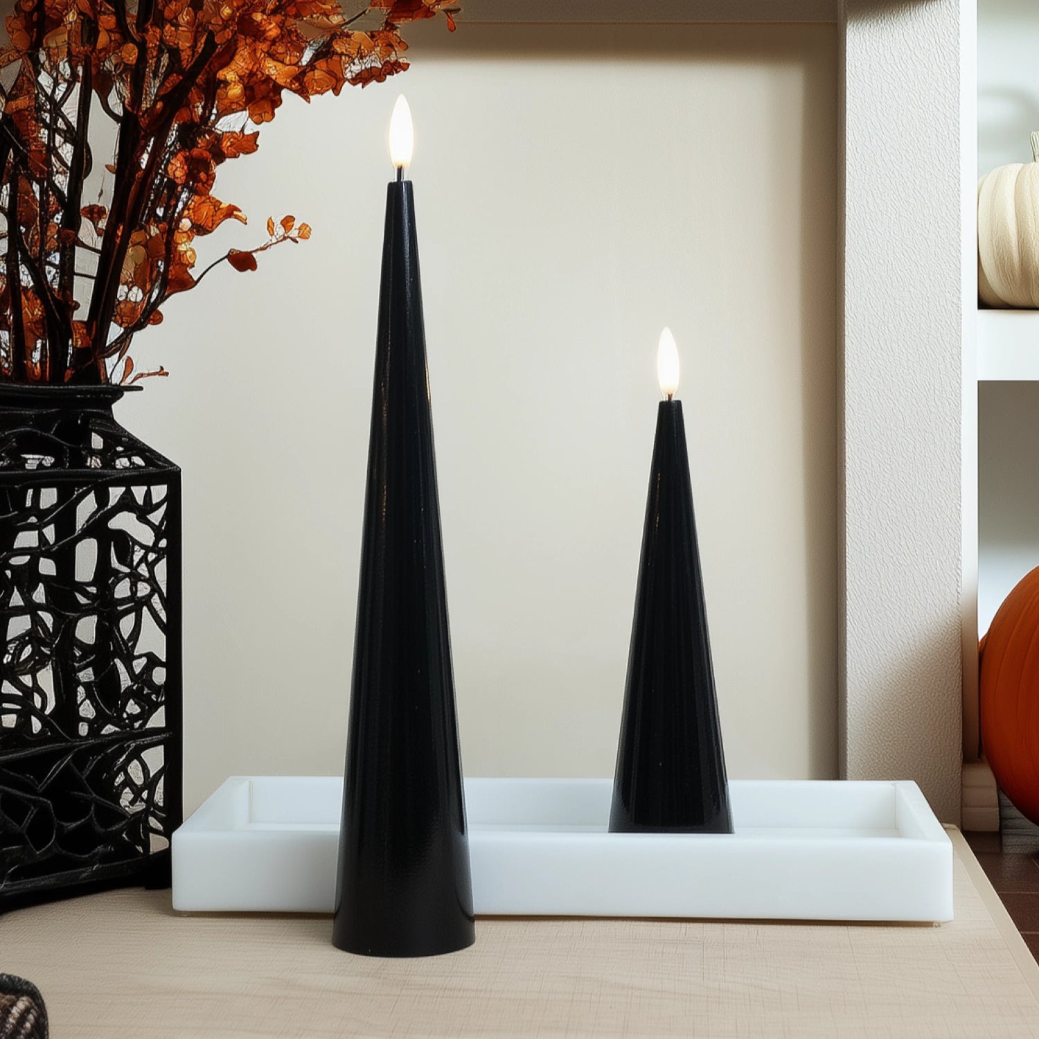 Two black taper candles on a white tray with decorative elements in the background.#color_shiny-black