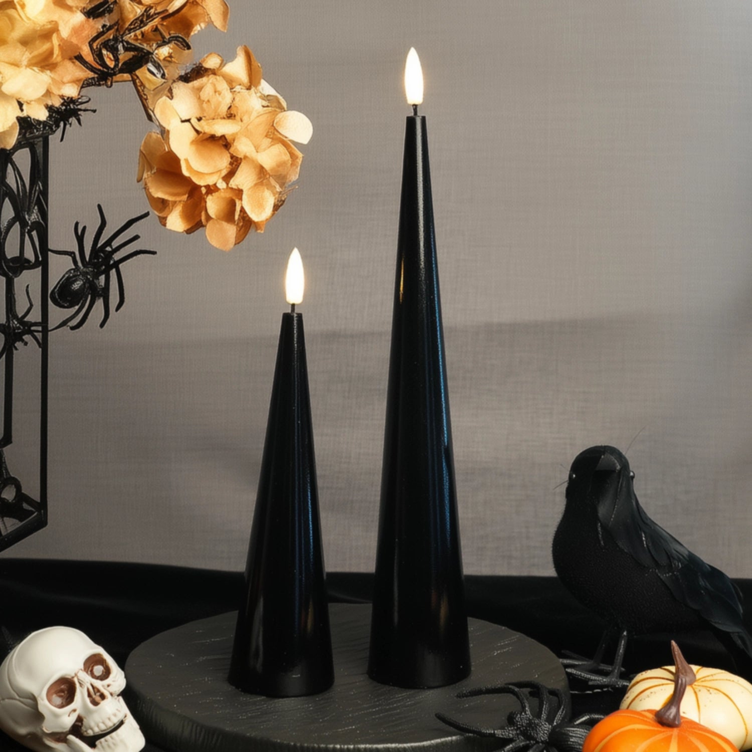 Black cone-shaped candles with lit flames on a table with Halloween decorations.