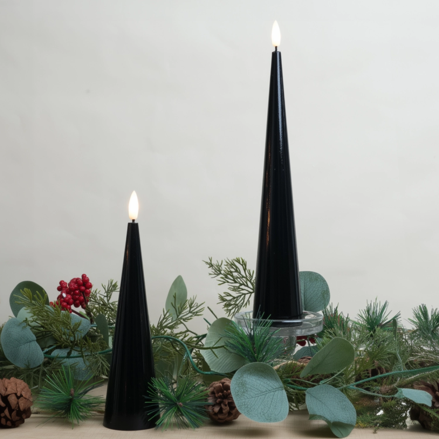 Two black candles with greenery on a light gray background#color_shiny-black