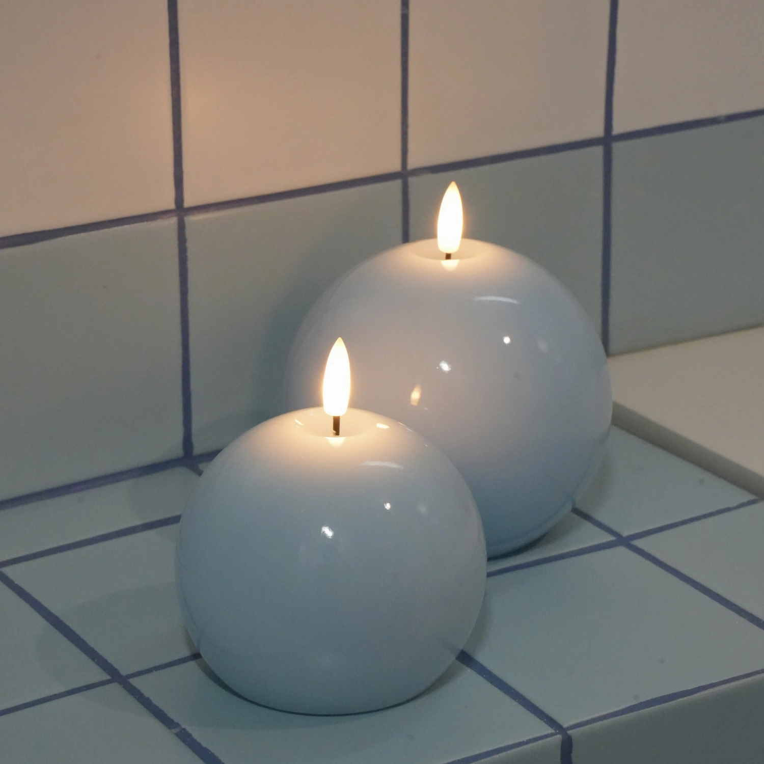 Two spherical white candles with lit wicks on a tiled surface.#color_shiny-blue