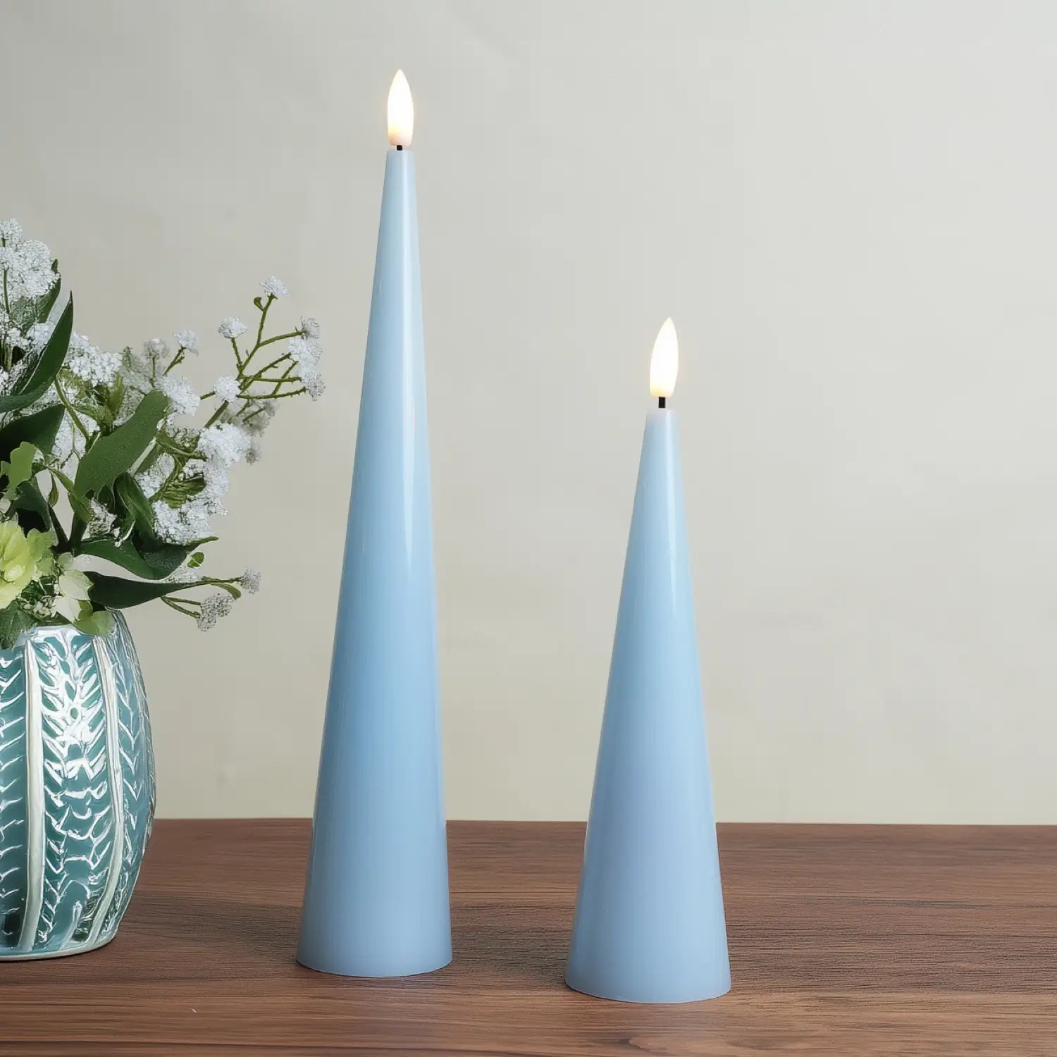 Two light blue cone-shaped candles with a vase of flowers on a wooden surface.#color_shiny-blue