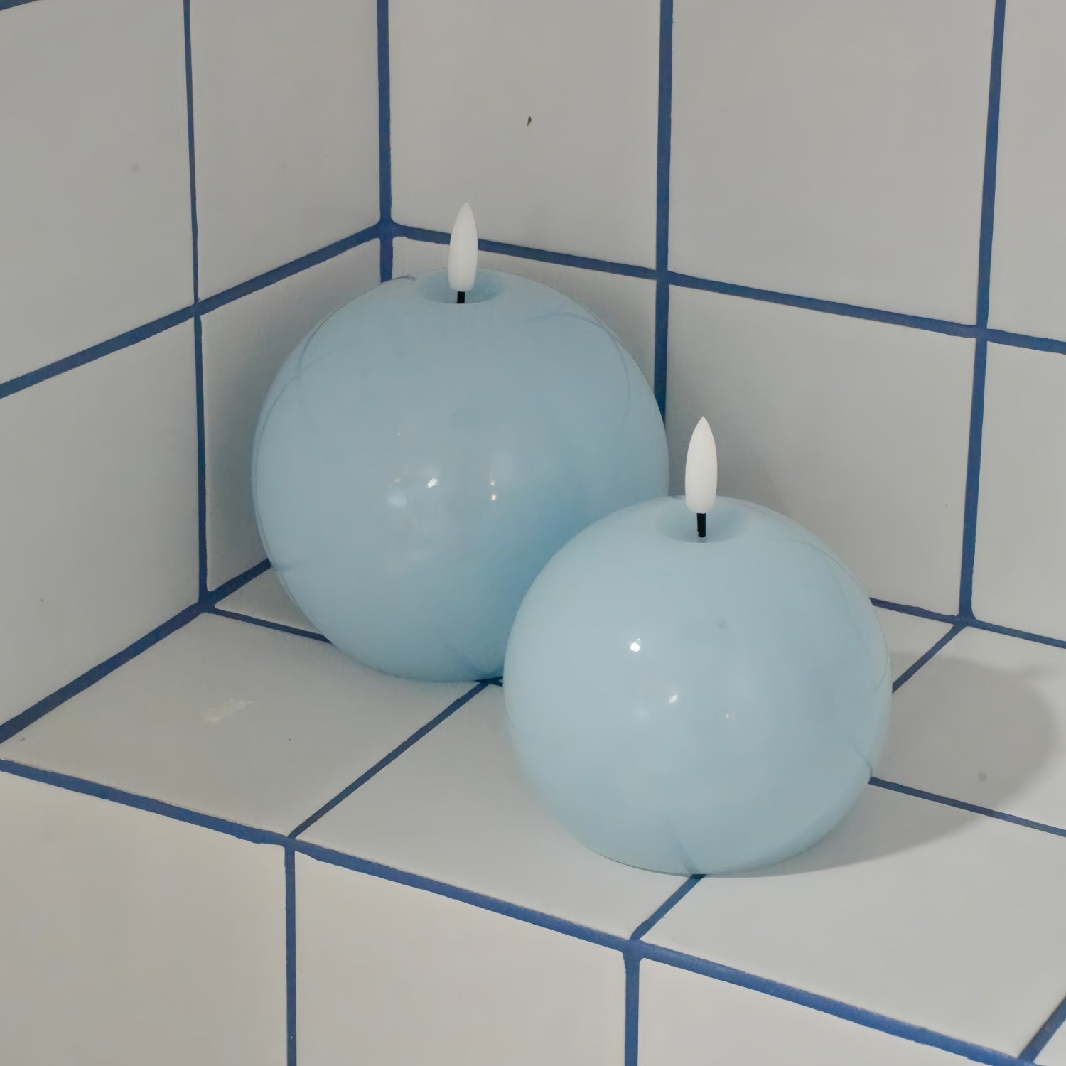 Two spherical candles with flames on a tiled bathroom counter.