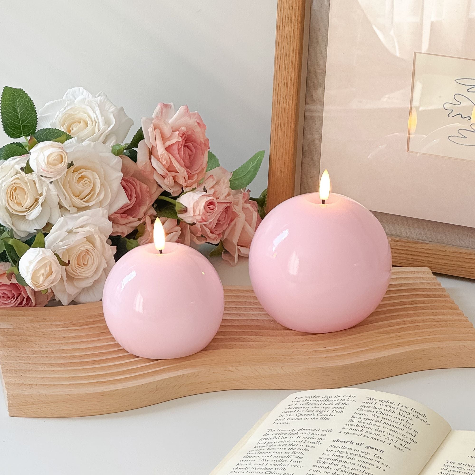 Two pink candles on a stack of books with a plant in the background#color_shiny-pink