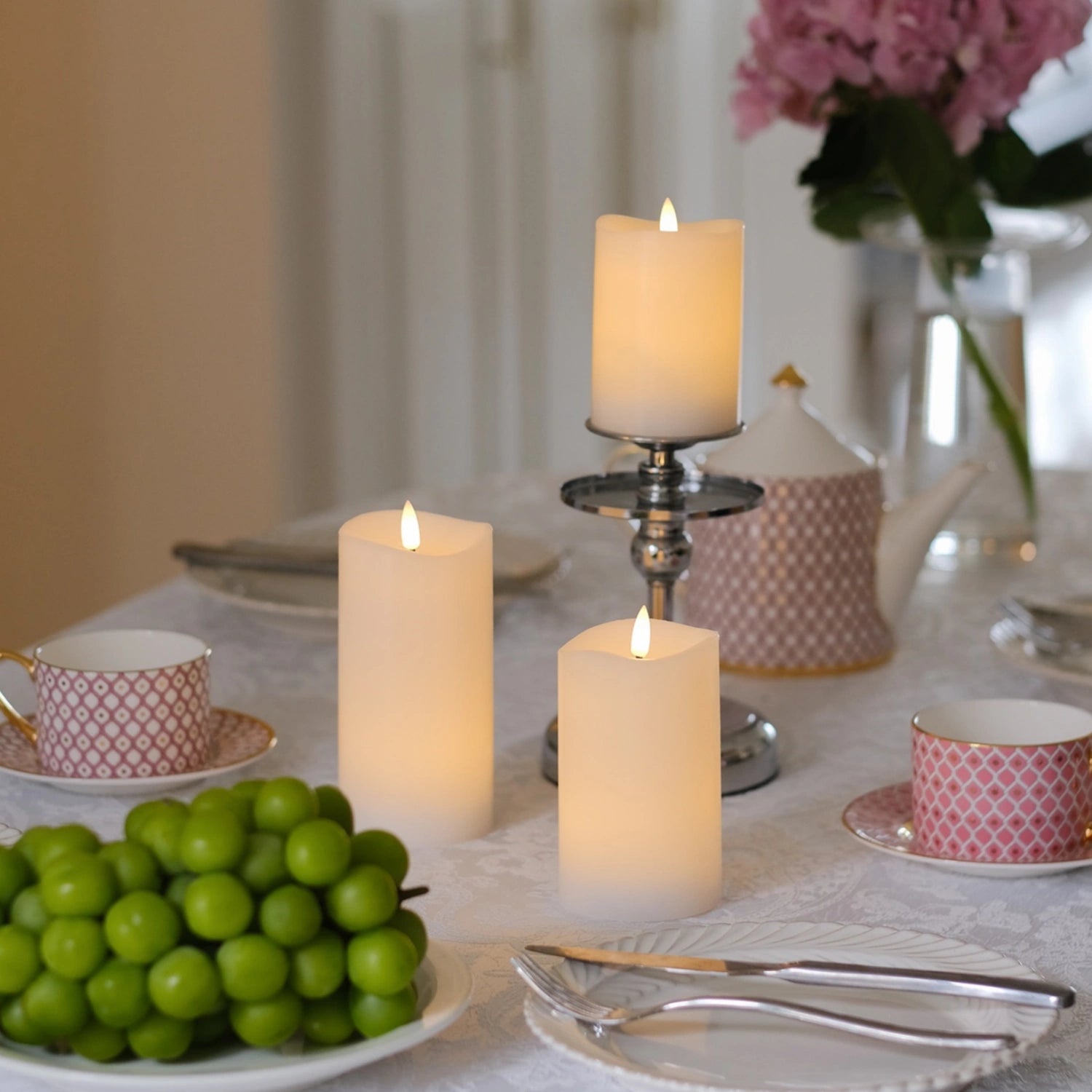 Decorative table setting with candles and greenery on a white tablecloth.