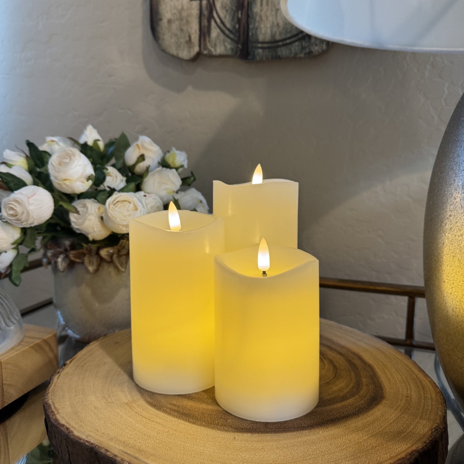 Three lit candles on a wooden surface with flowers in the background
