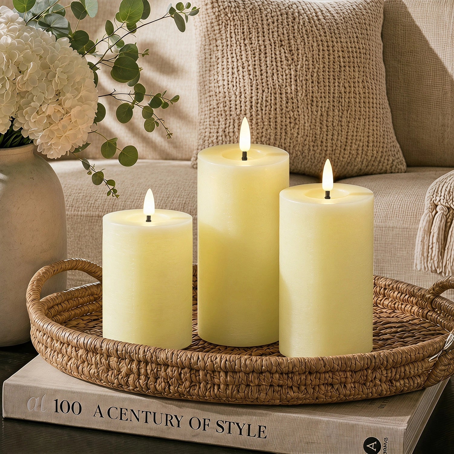 Three lit candles on a woven tray with a book titled 'A Century of Style' in the background.#color_rustic-ivory