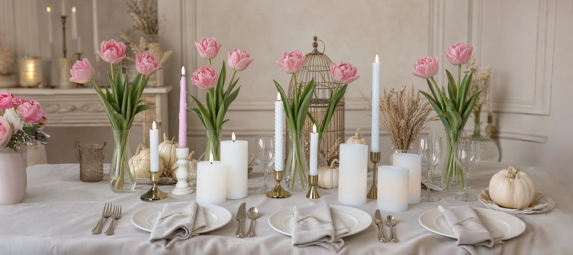 Elegant dining table setting with pink tulips, candles, and decorative items in a softly lit room.