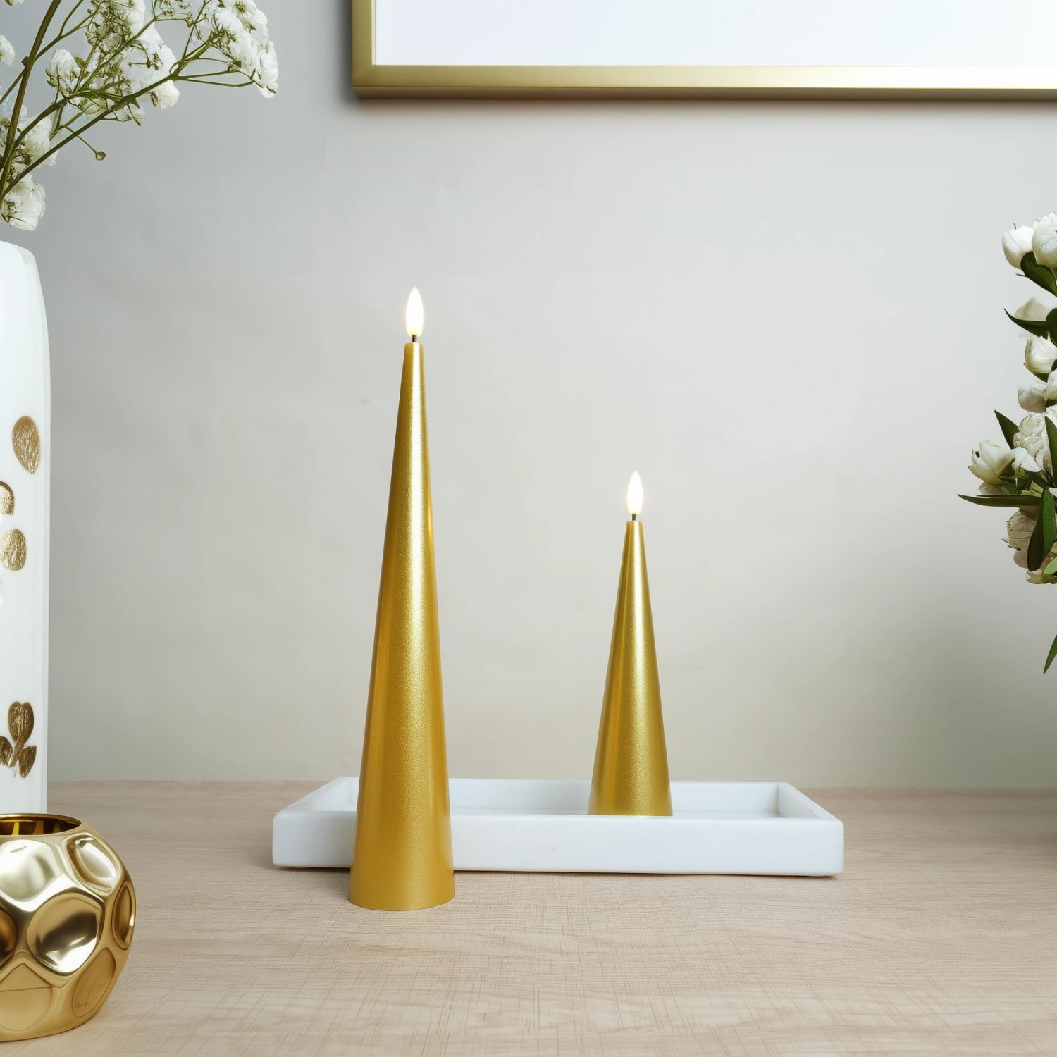 Two gold candles on a white tray with decorative elements on a wooden surface.