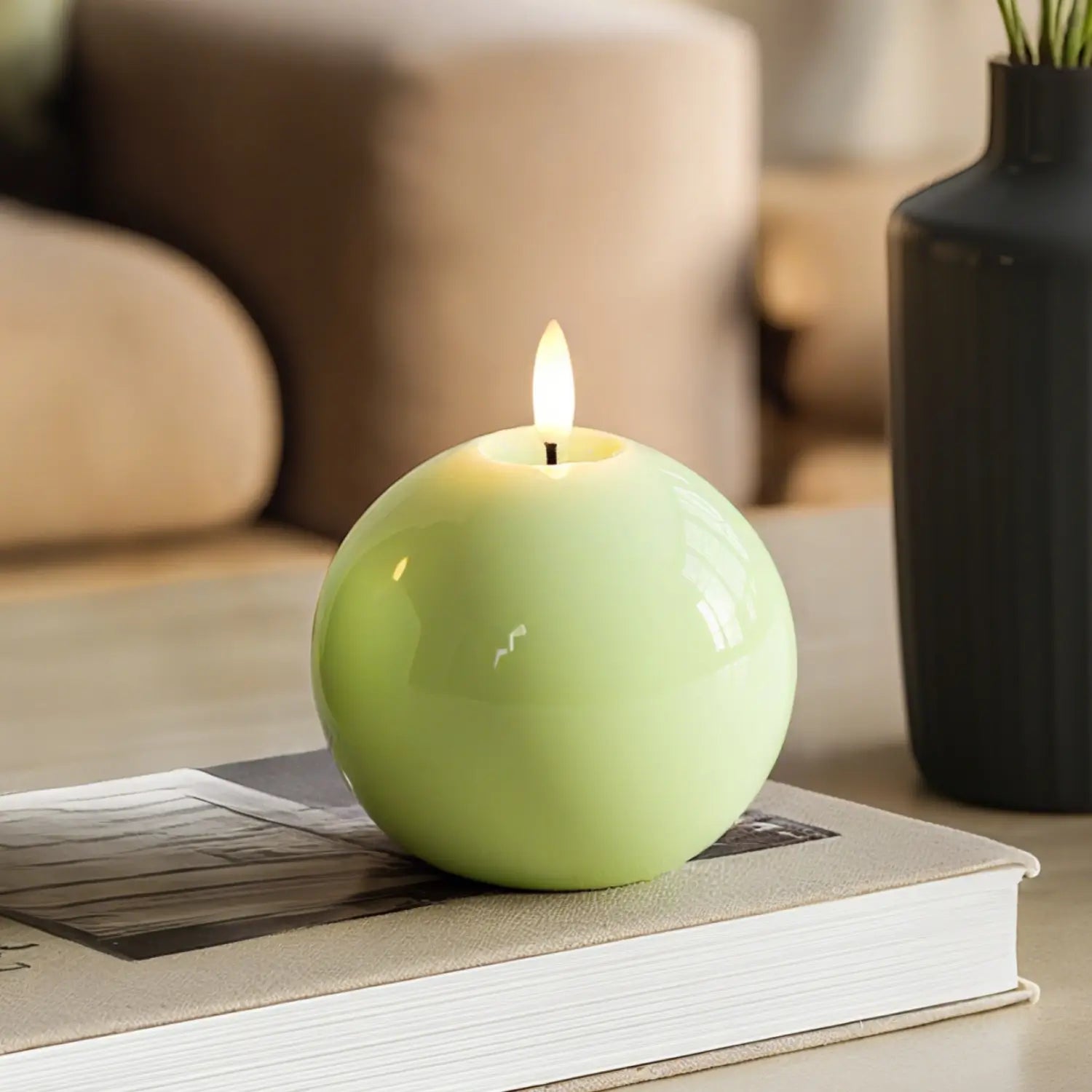Green spherical candle with a flame on a book in a cozy indoor setting#color_shiny-green