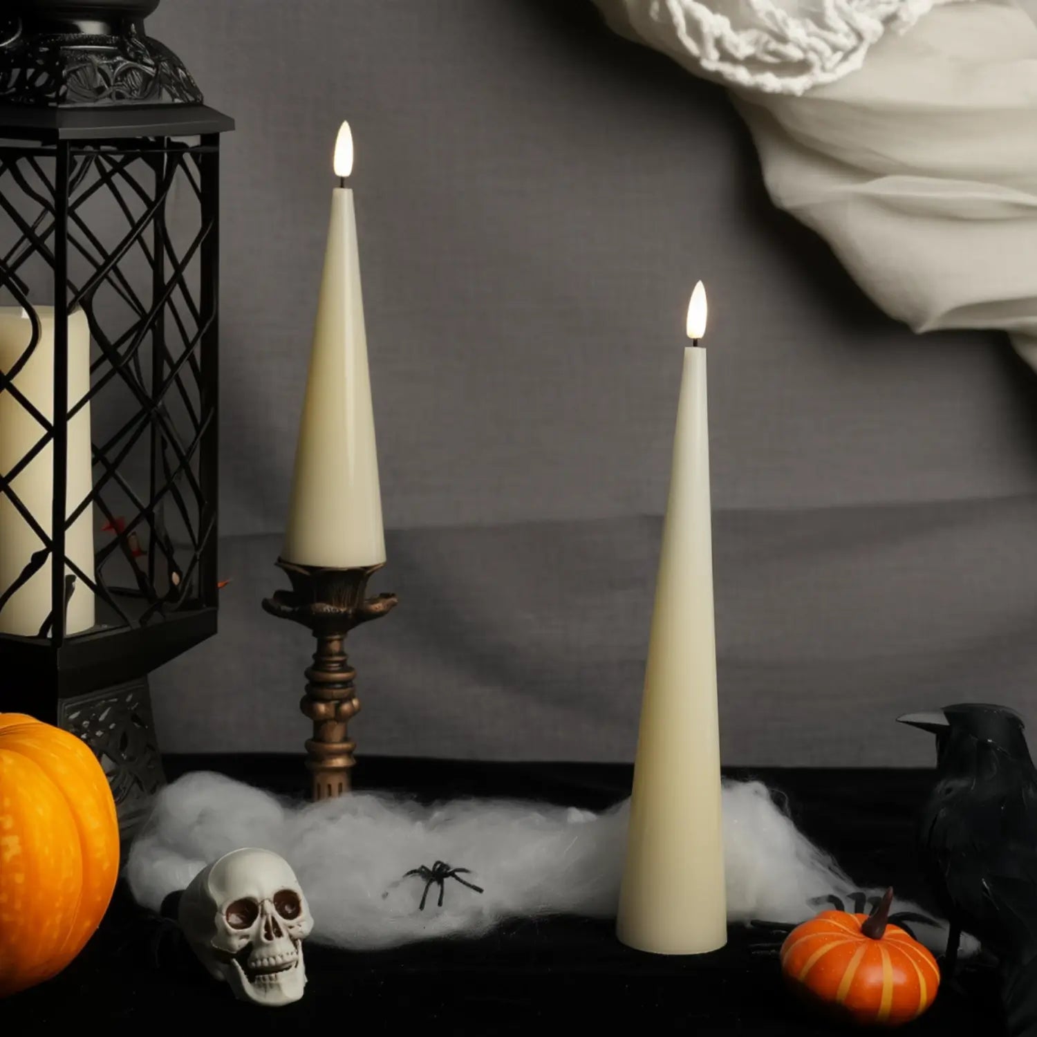 Halloween-themed arrangement with candles, pumpkins, a skull, and a spider on a dark background.#color_shiny-ivory