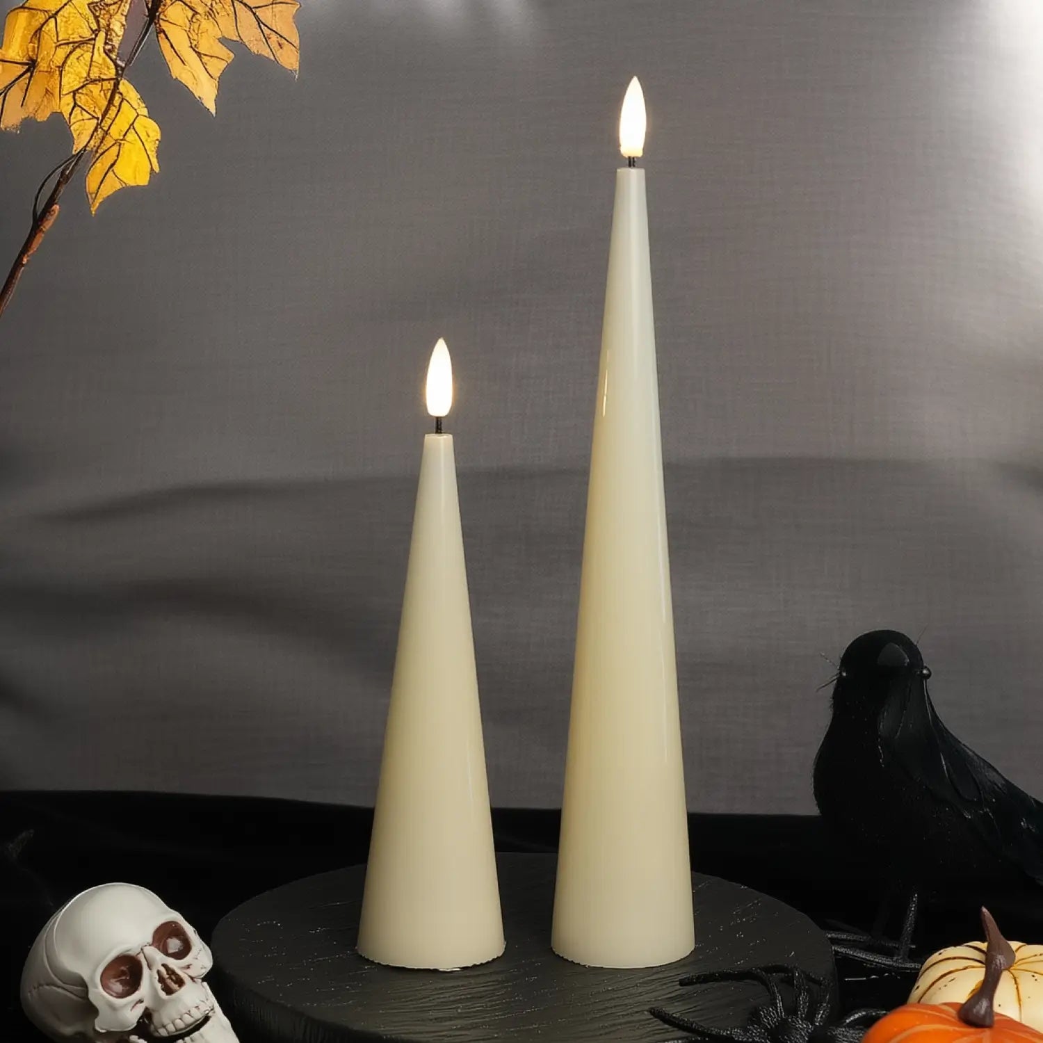 Two white cone-shaped candles with lit wicks on a dark surface with a gray background.