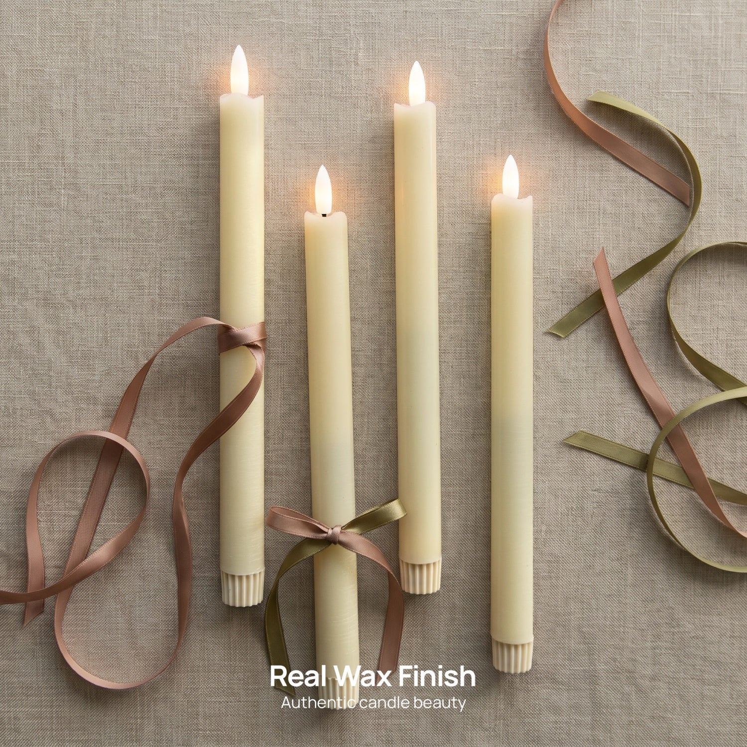 Four cream-colored real wax taper candles with lit flames, tied with brown and olive ribbons, arranged on a textured beige linen background with matching ribbon curls.#color_rustic-ivory