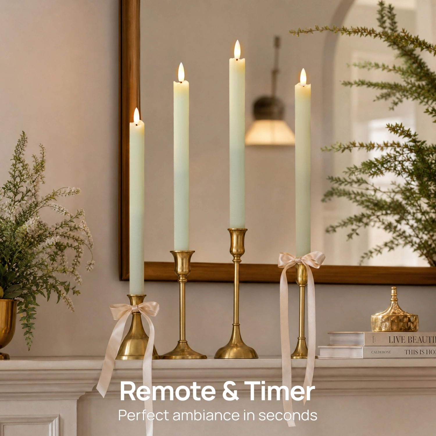 Four tall white taper candles in brass candlesticks arranged on a mantel, with two tied in cream ribbons and lit candles above. A mirror, framed wall art, books, and greenery decorate the background.