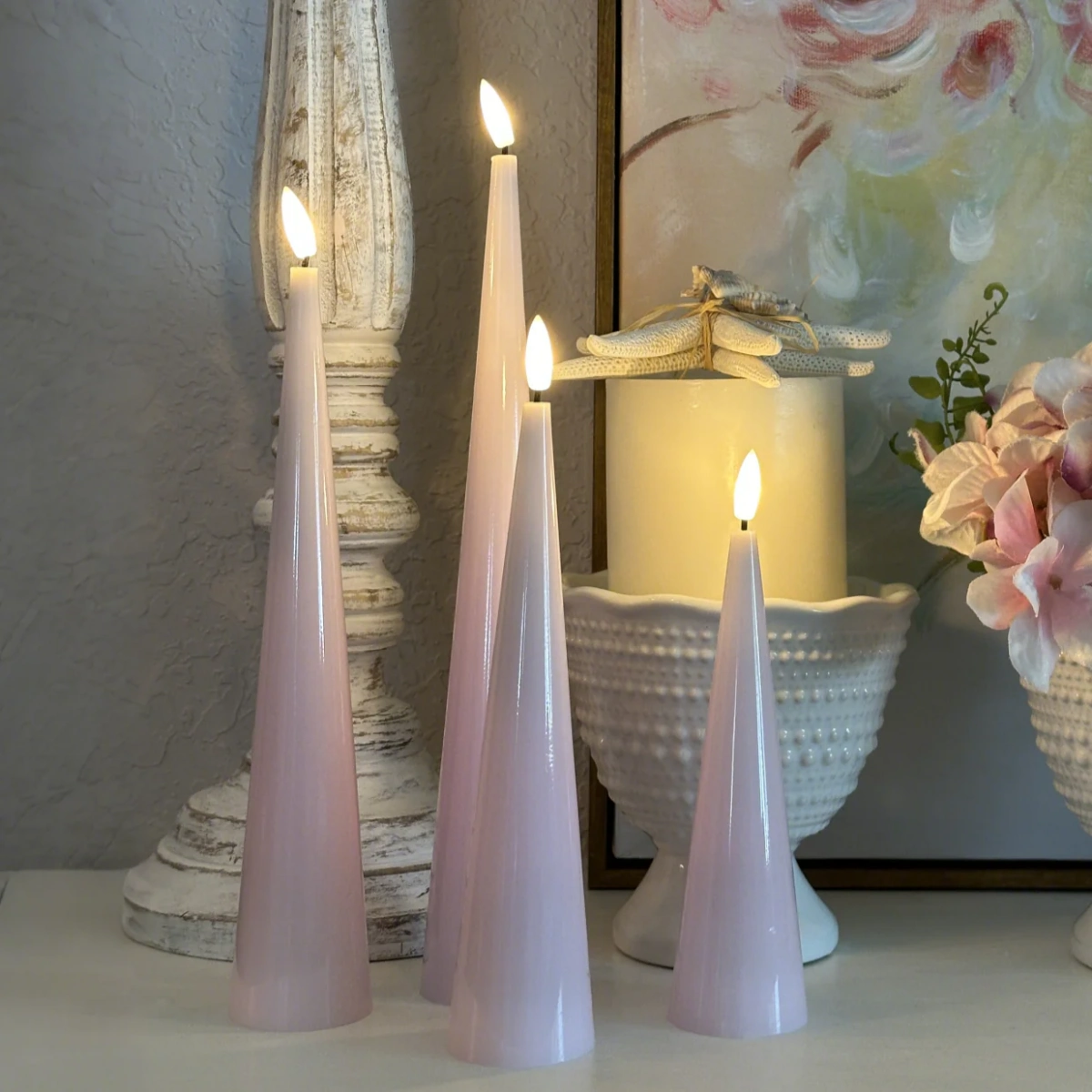Set of three pink candles on a surface with decorative items in the background#color_shiny-pink