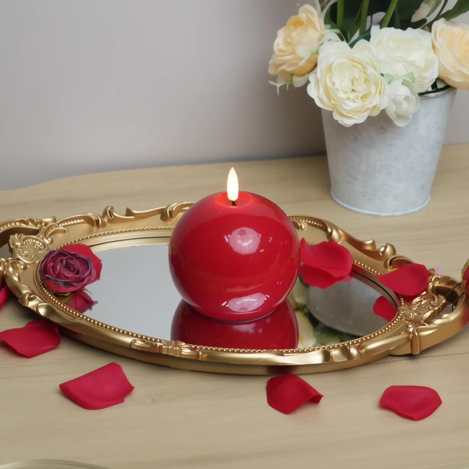 Red spherical candle on a wooden base with a Christmas tree and gift in the background#color_shiny-red