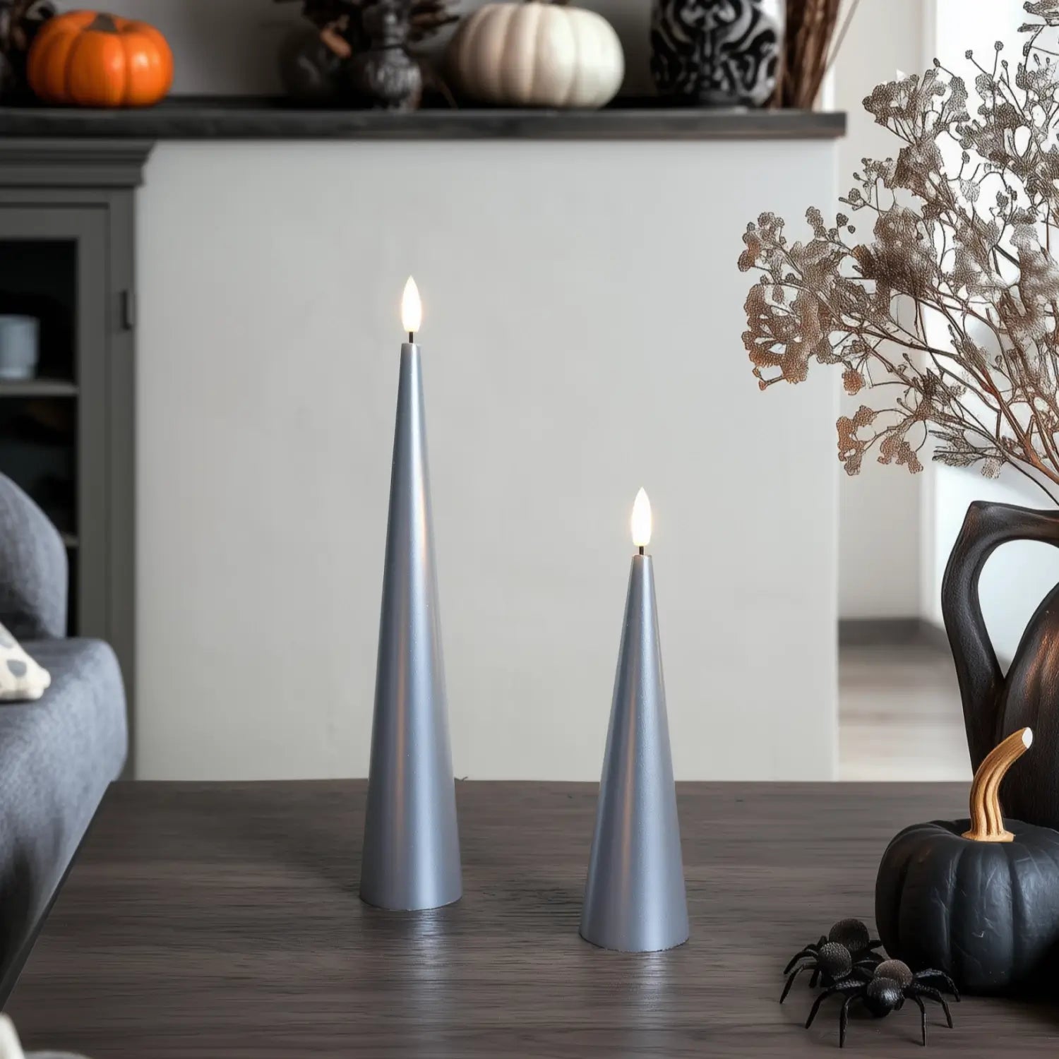 Two lit silver candles on a wooden surface with decorative elements in the background.#color_lacquered-silver