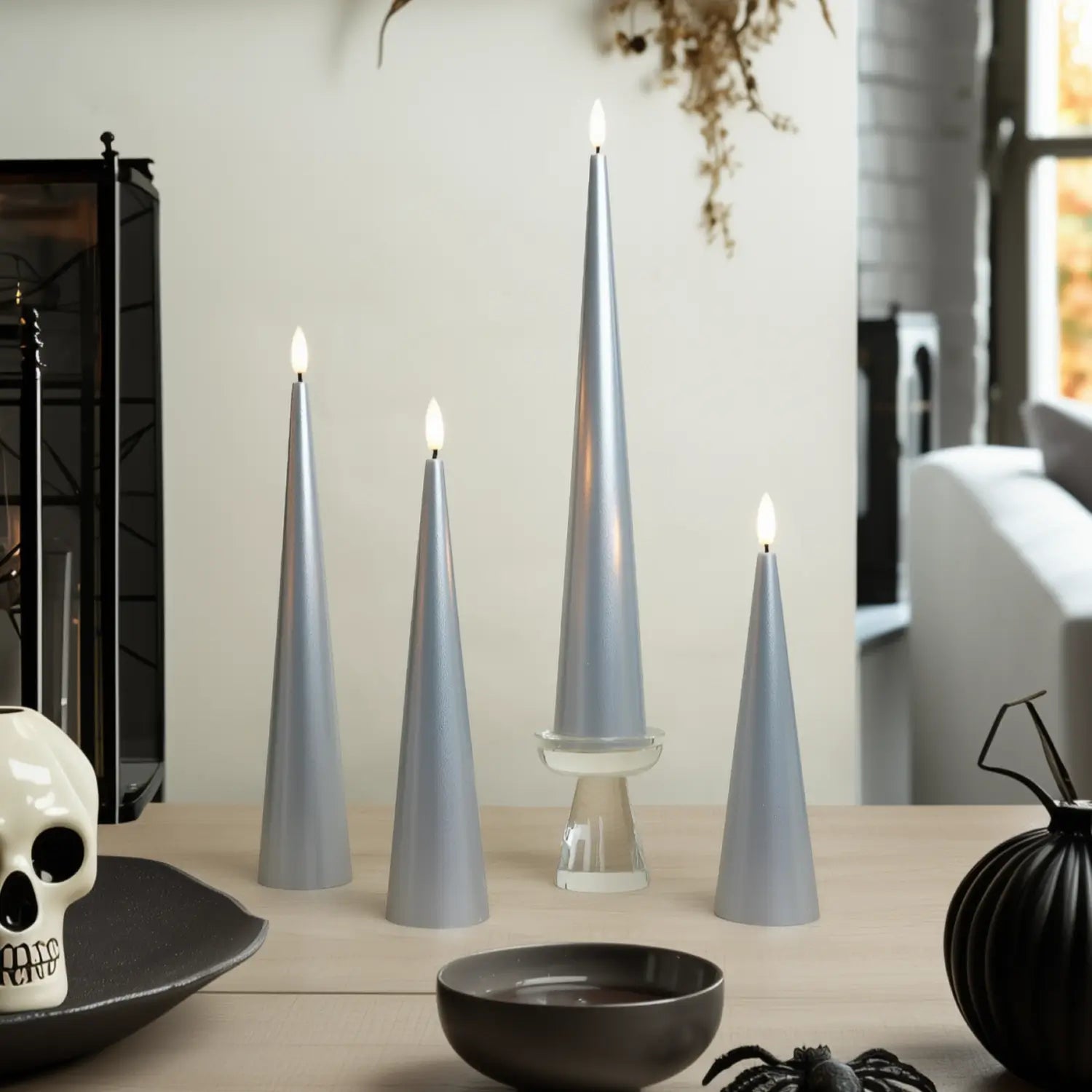 Set of silver cone-shaped candles on a table with decorative items.#color_lacquered-silver