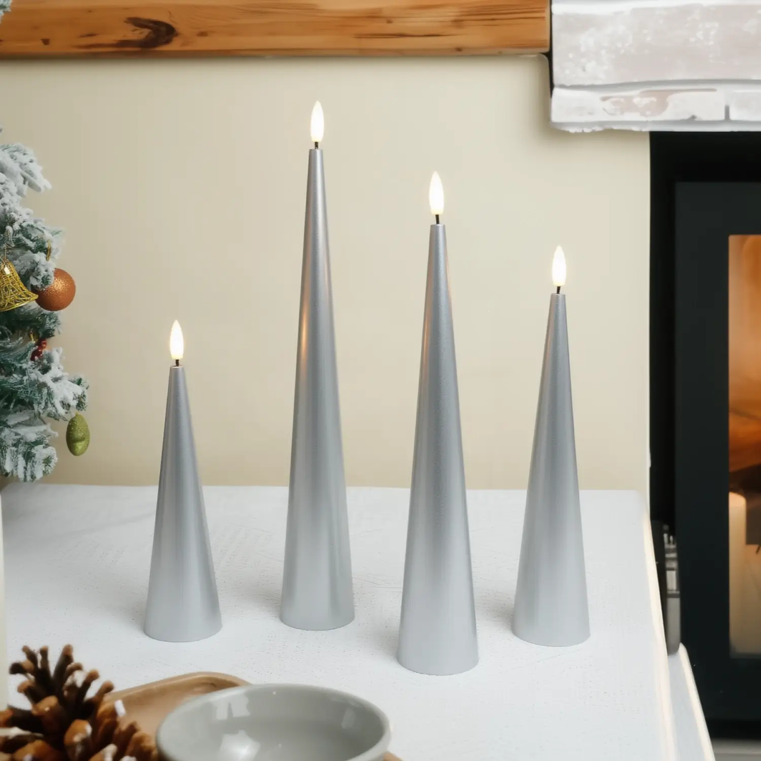 Set of four gray cone-shaped candles on a table with a fireplace and Christmas decorations in the background.#color_lacquered-silver