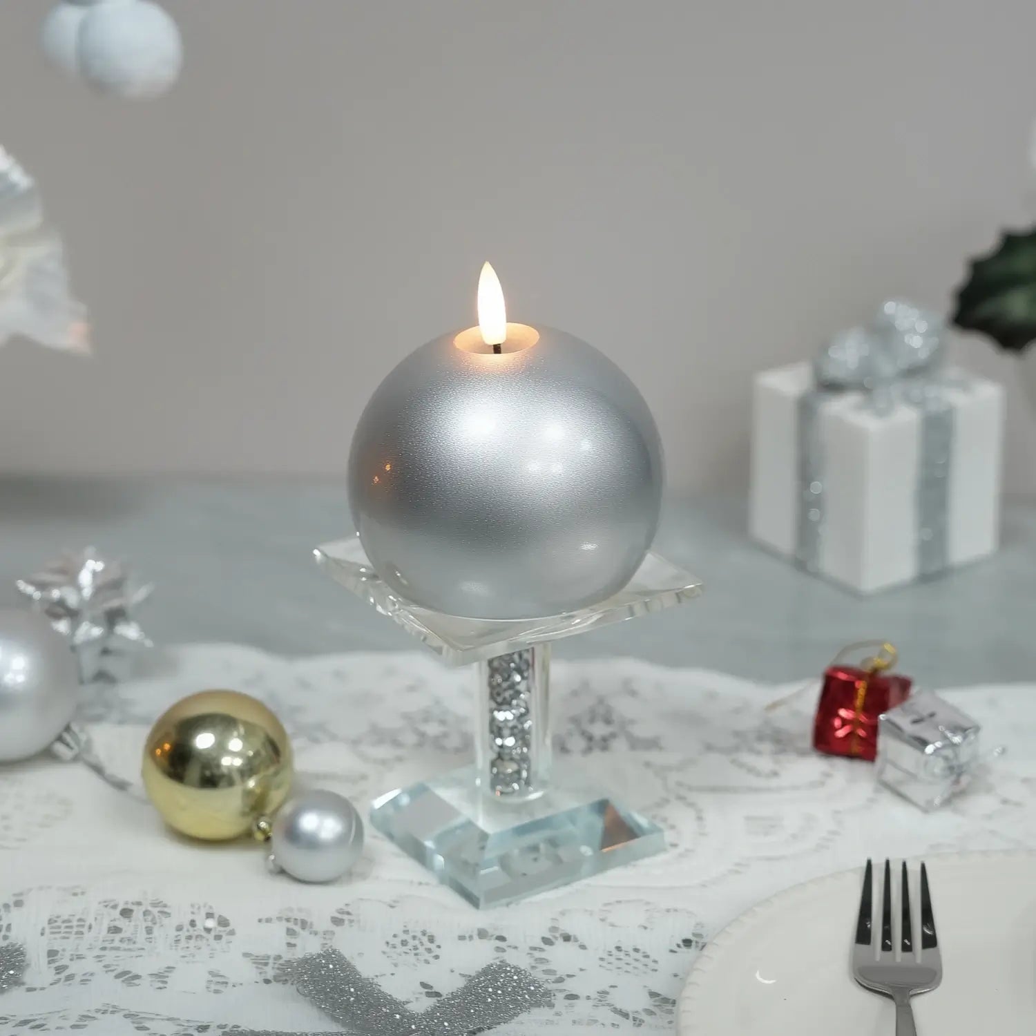 Silver ball candle surrounded by greenery and pine cones on a neutral background#color_lacquered-silver