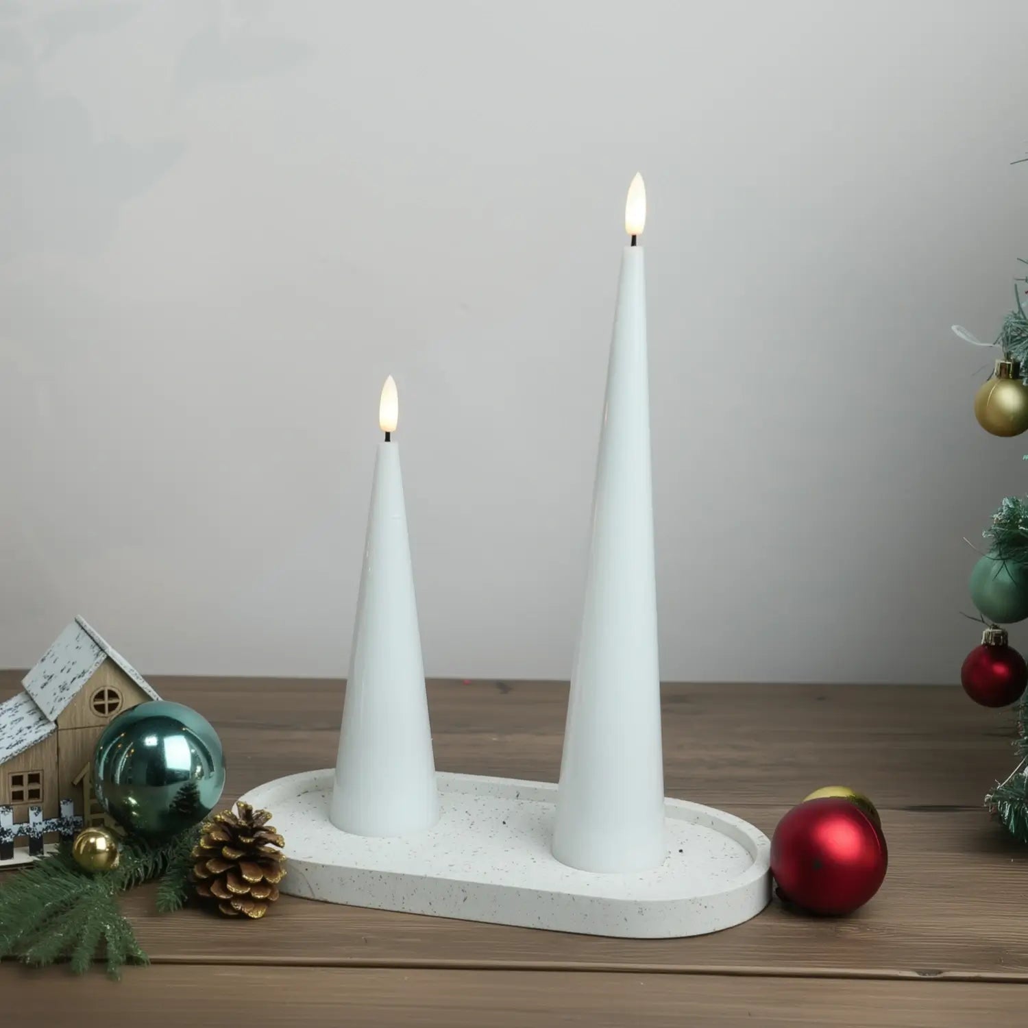 Two white candles on a table with greenery and a decorative pillow in the background#color_shiny-white