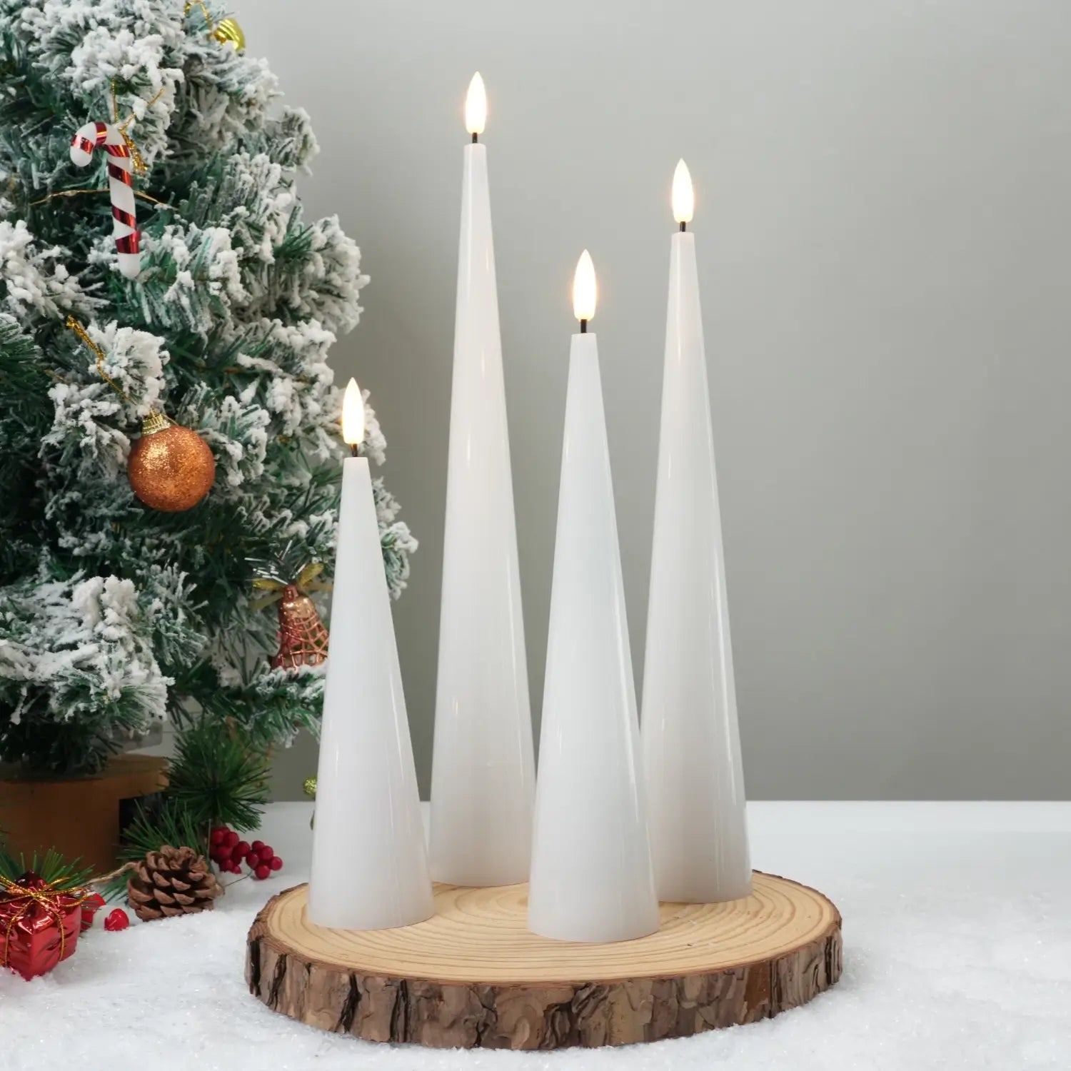 White candles on a wooden base with a Christmas tree in the background