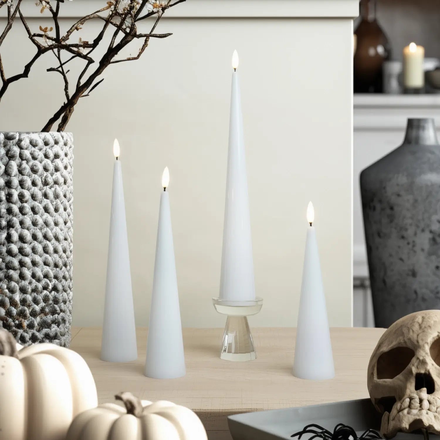 Decorative setup with white candles, pumpkins, and a skull on a neutral background