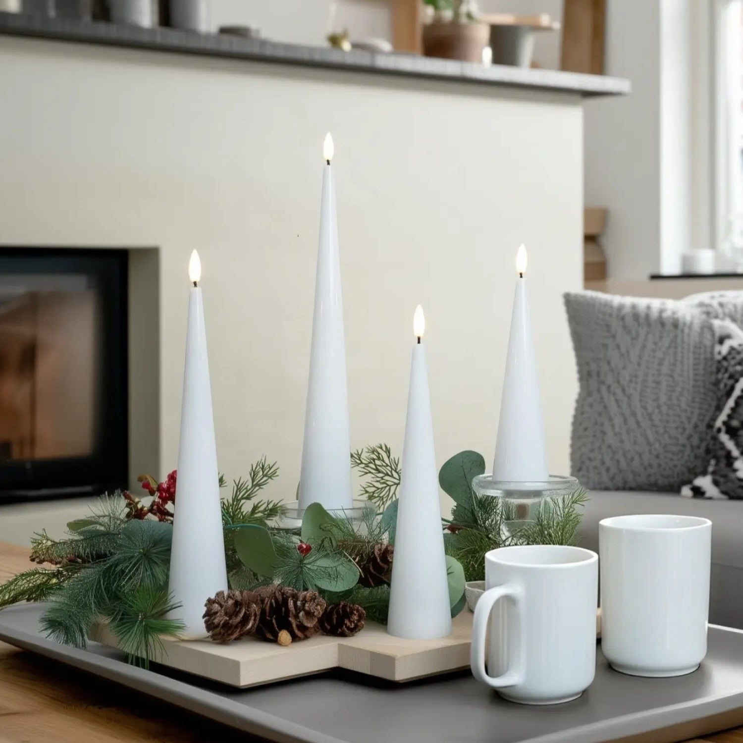 White candles and mugs on a tray with a fireplace and sofa in the background