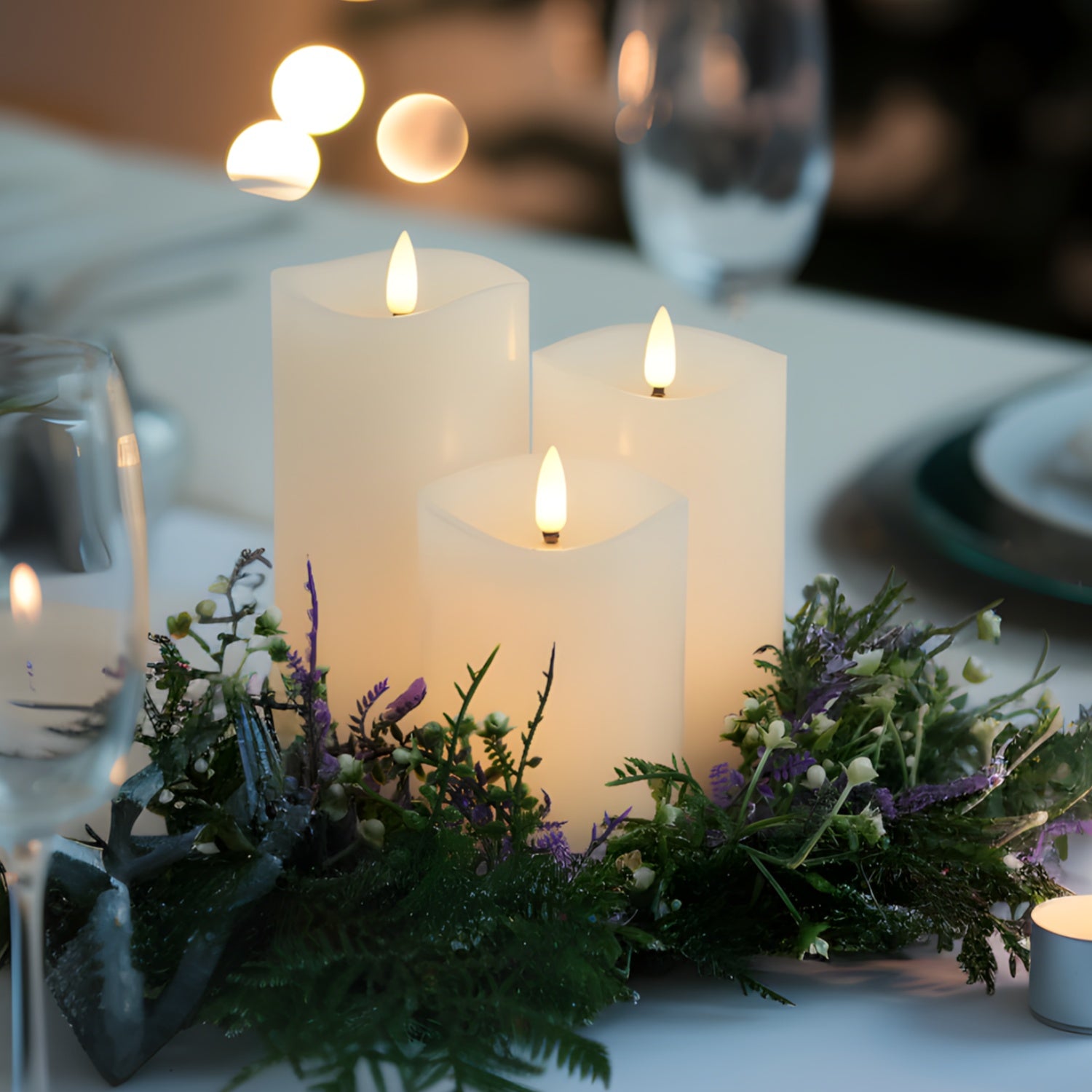 Decorative table setting with candles and greenery on a white tablecloth.