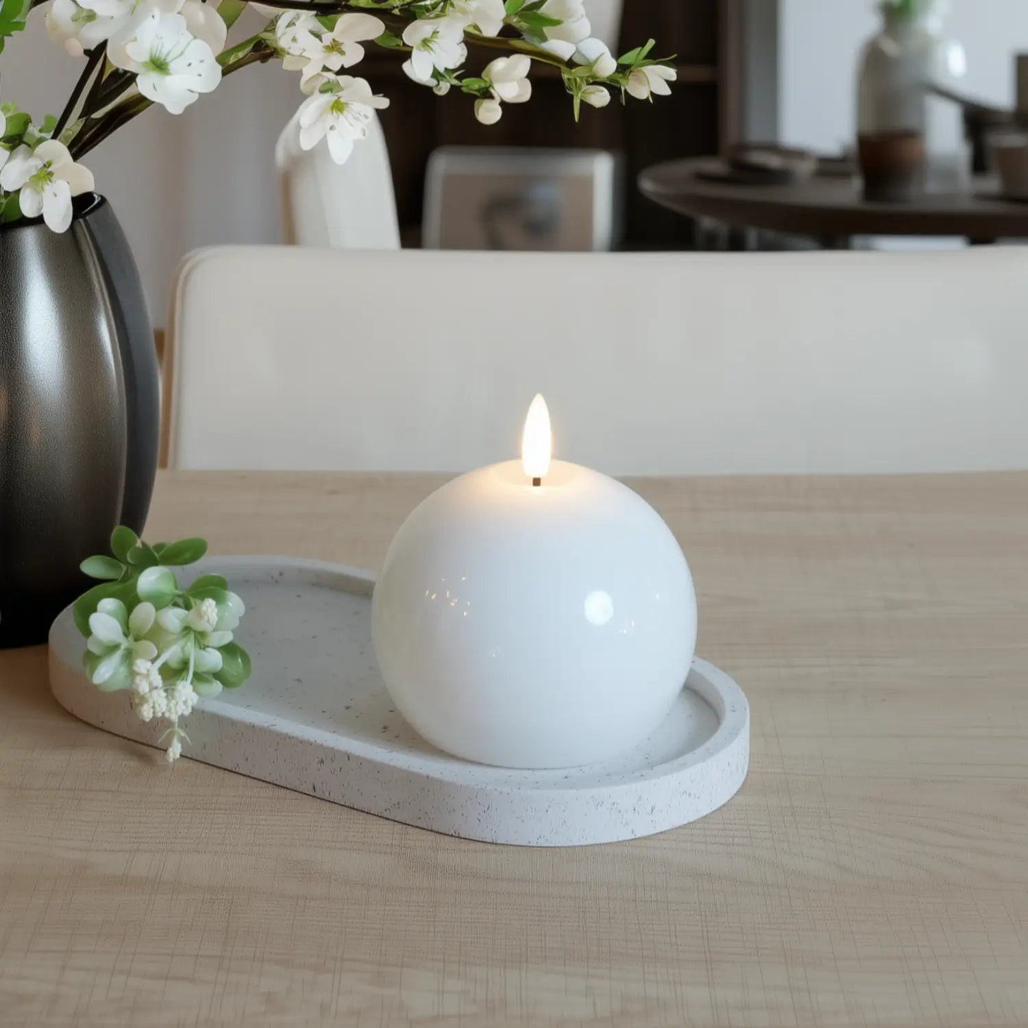 White spherical candle on a concrete tray with flowers on a wooden table#color_shiny-white