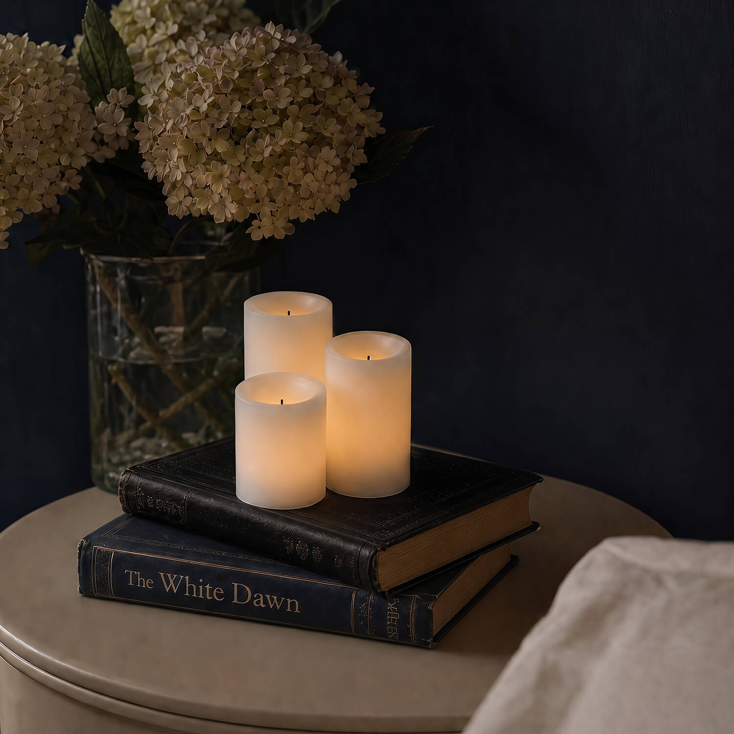 Three lit candles on top of two books with a vase of flowers in the background.