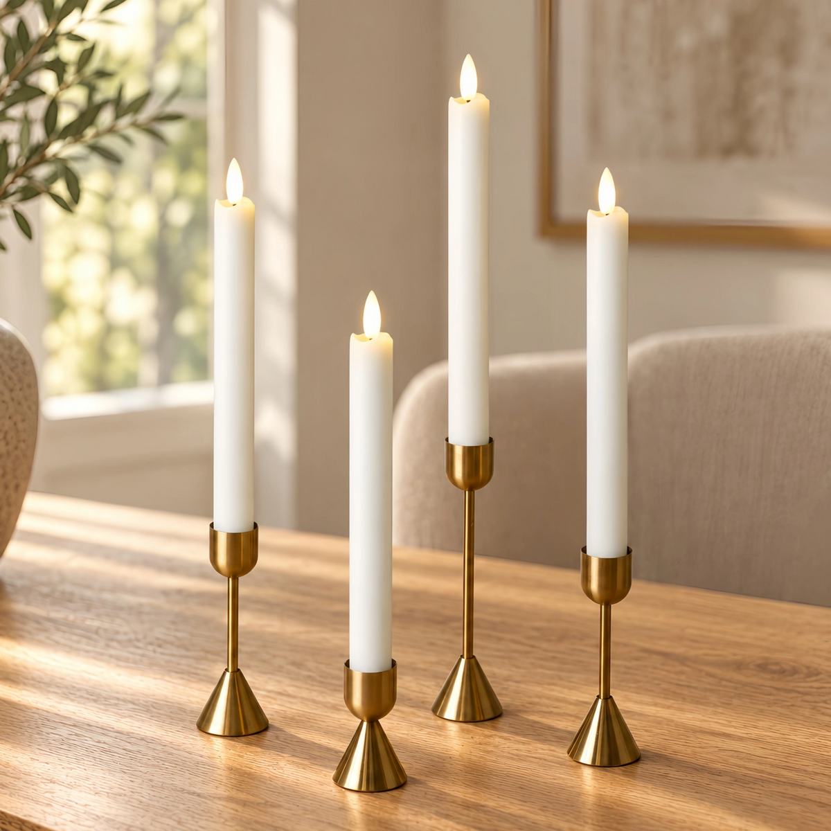 Four white taper candles in slim gold metal holders arranged on a wooden table in a softly lit room.#color_rustic-white