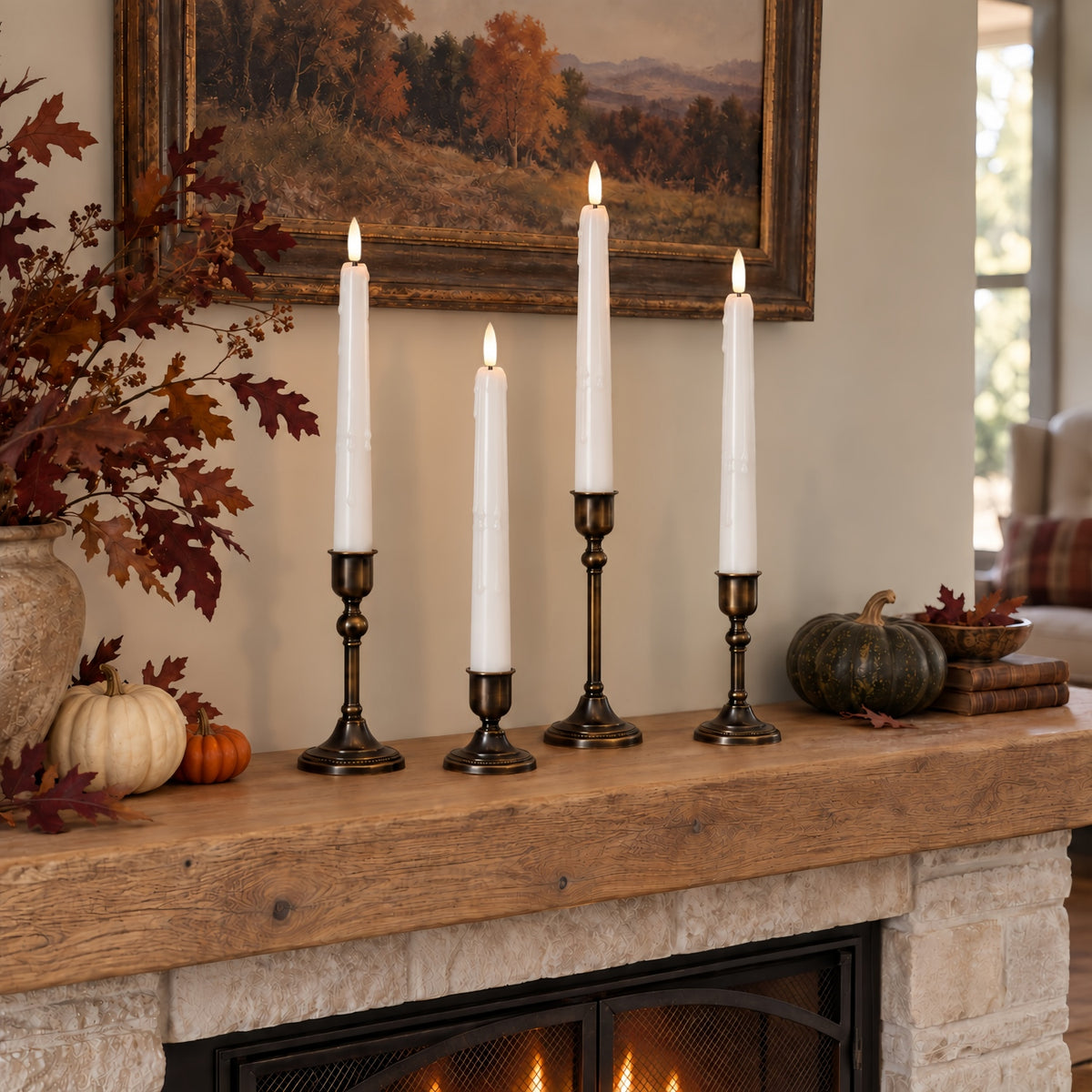 Four white taper candles in dark metal candlesticks displayed on a rustic wooden fireplace mantel in a cozy living room setting.