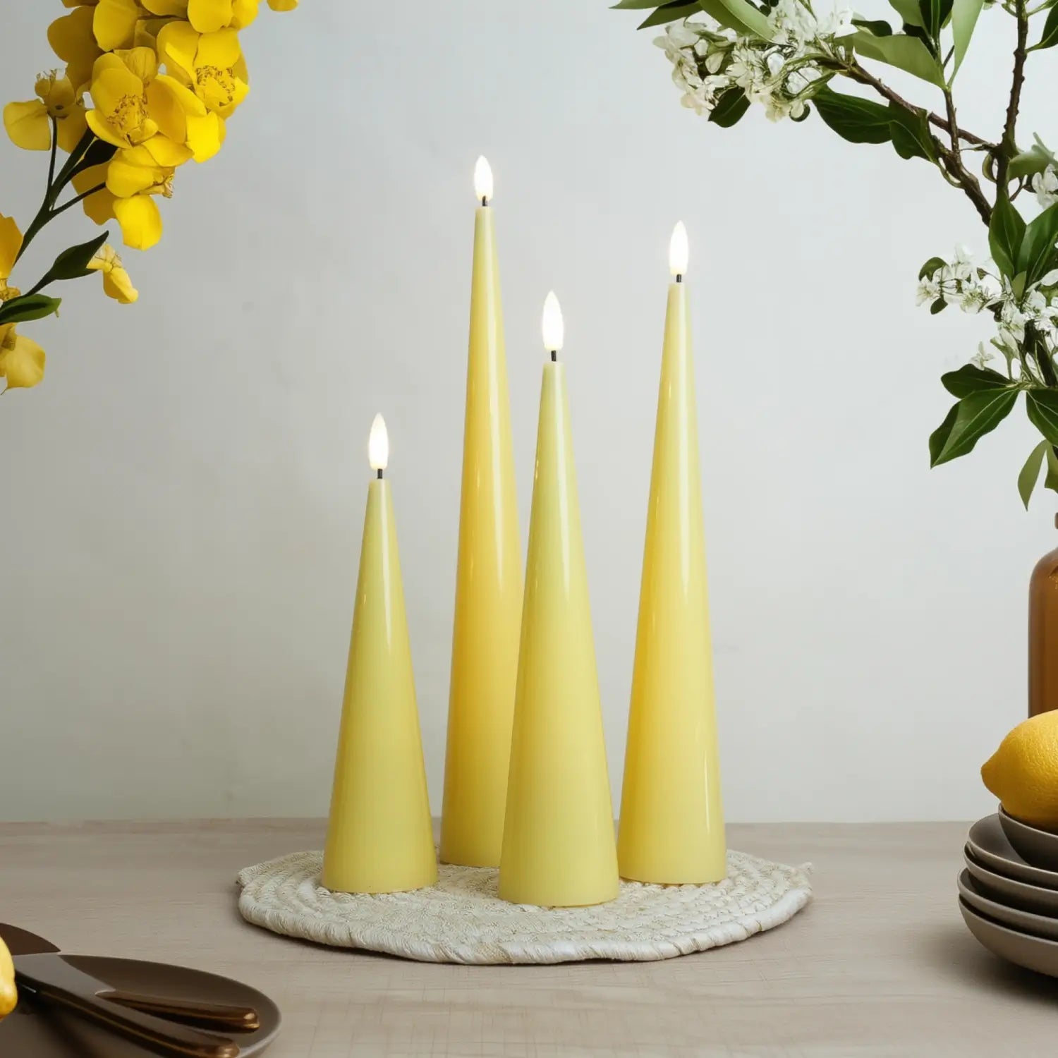 Yellow candles on a woven mat with flowers and lemons in the background#color_shiny-yellow