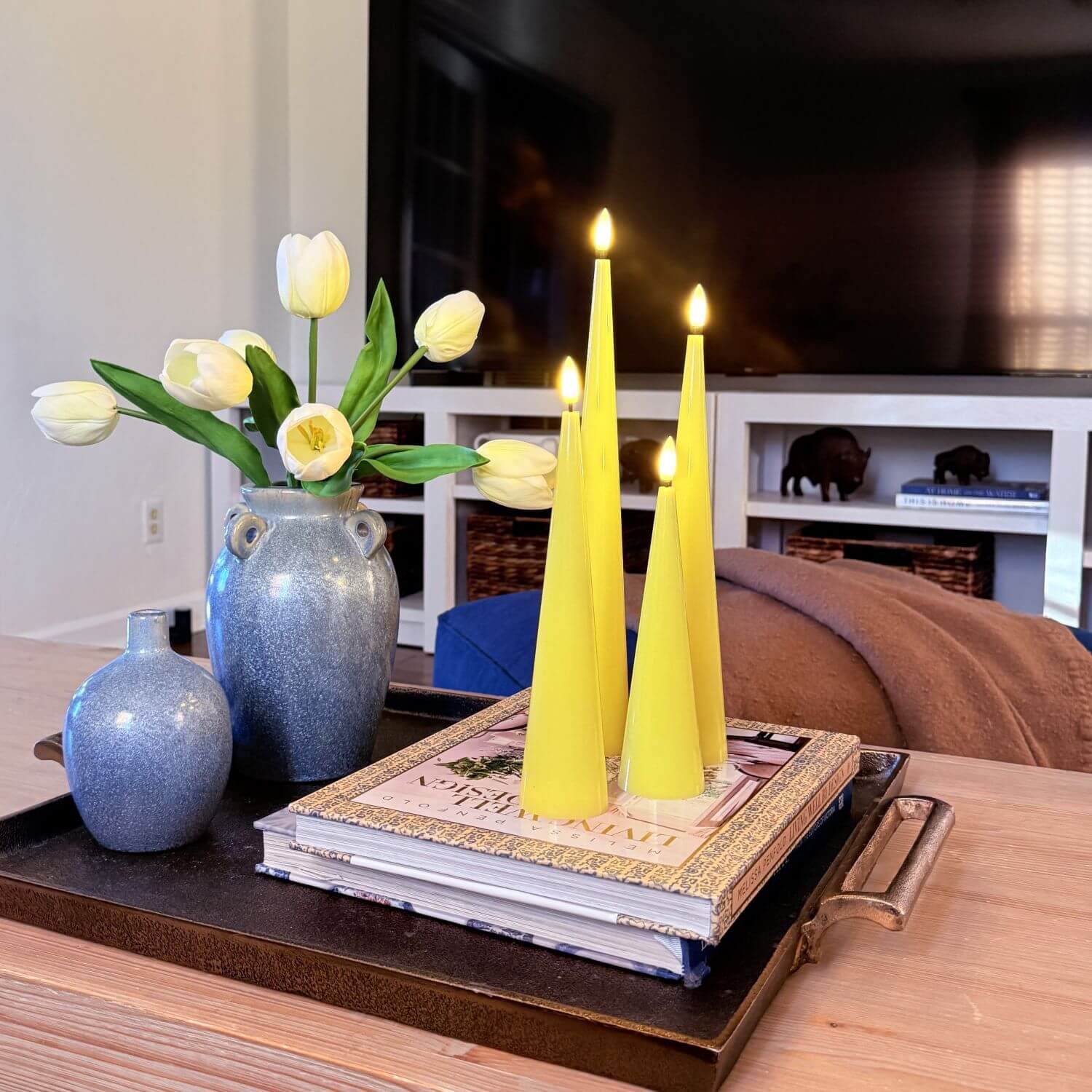 Set of four yellow taper candles on a wooden surface with a neutral background
