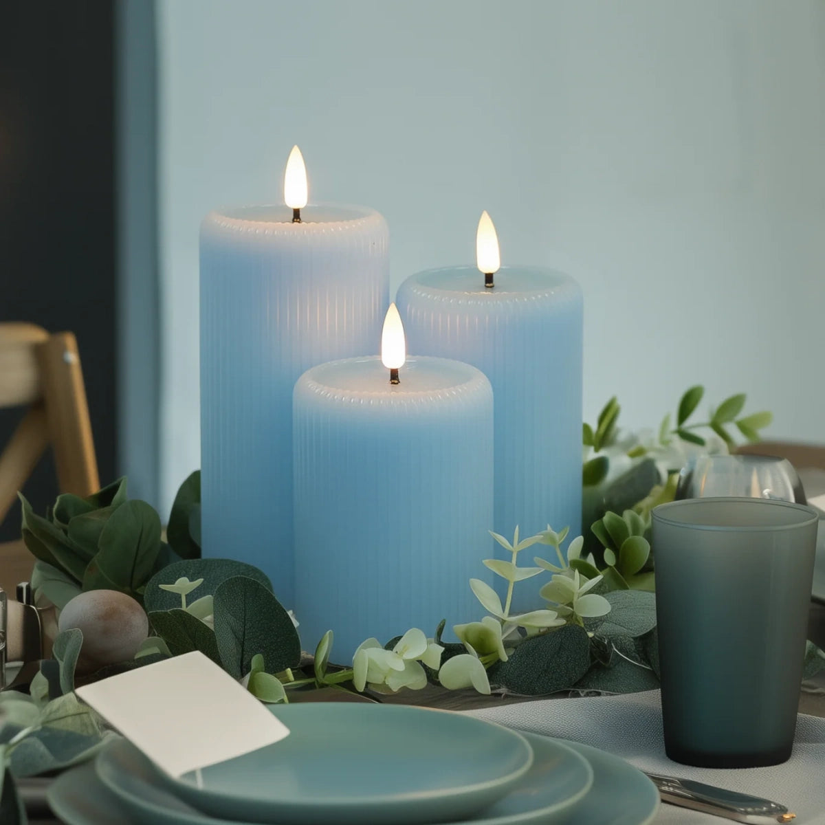 Three blue candles on a table with greenery and dinnerware.
