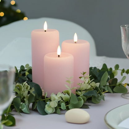 Three pink candles on a bed of greenery with a blurred background