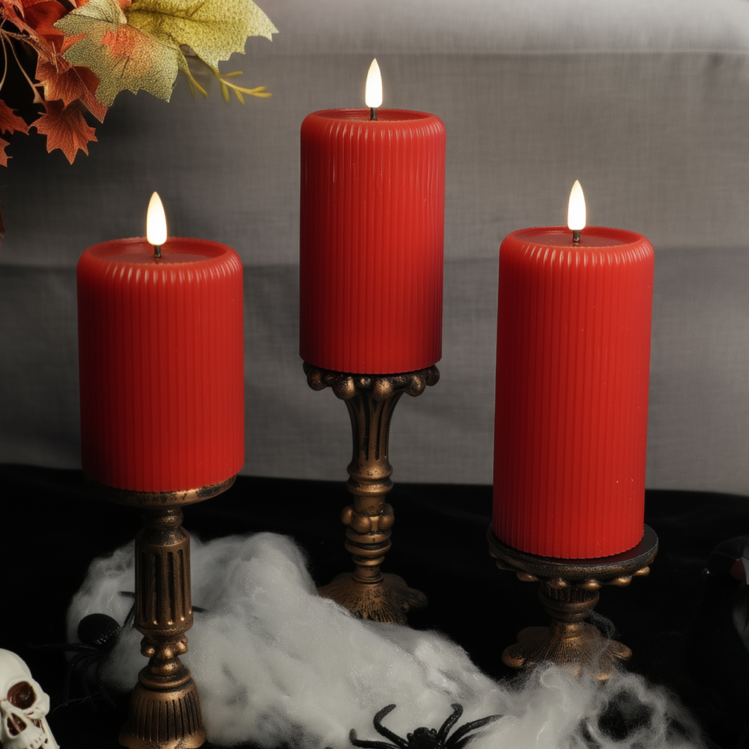 Three red candles on decorative stands with Halloween-themed decorations including a skull and spider.#color_red