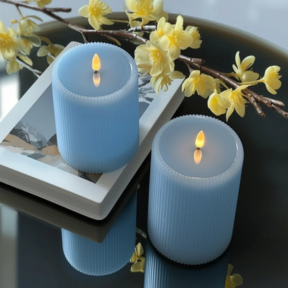 Two blue candles with yellow flames on a dark surface with yellow flowers in the background.