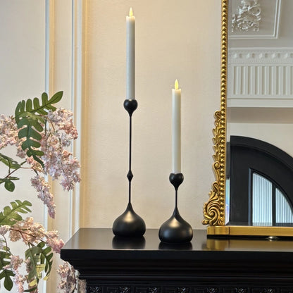 Two black candle holders with lit candles on a mantelpiece next to a decorative mirror.