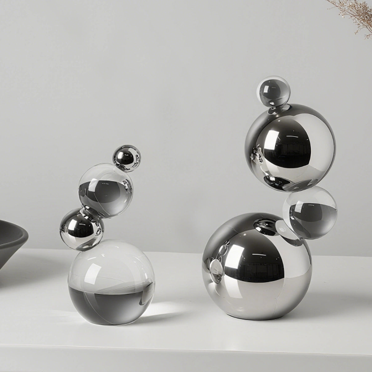 Set of silver and clear glass spherical sculptures on a light gray surface with a neutral background