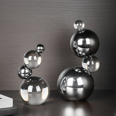 Decorative sculpture of stacked metallic spheres on a reflective surface with a dark background