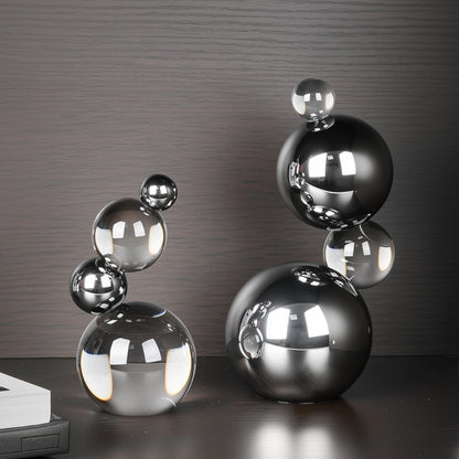 Decorative sculpture of stacked metallic spheres on a reflective surface with a dark background