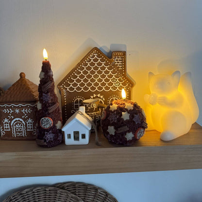 Decorative candles on a wooden base with a Christmas tree in the background