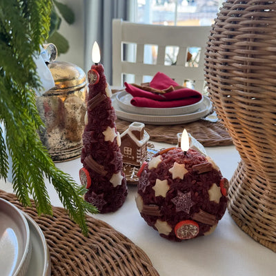 Decorative candles on a wooden base with a Christmas tree in the background