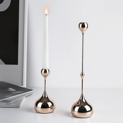 Two metallic candle holders with candles on a light gray surface.